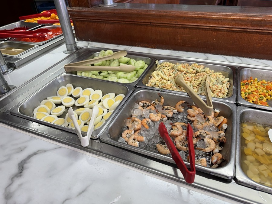 Steam table trays on a buffet line filled with shrimp, noodles, eggs and other dishes